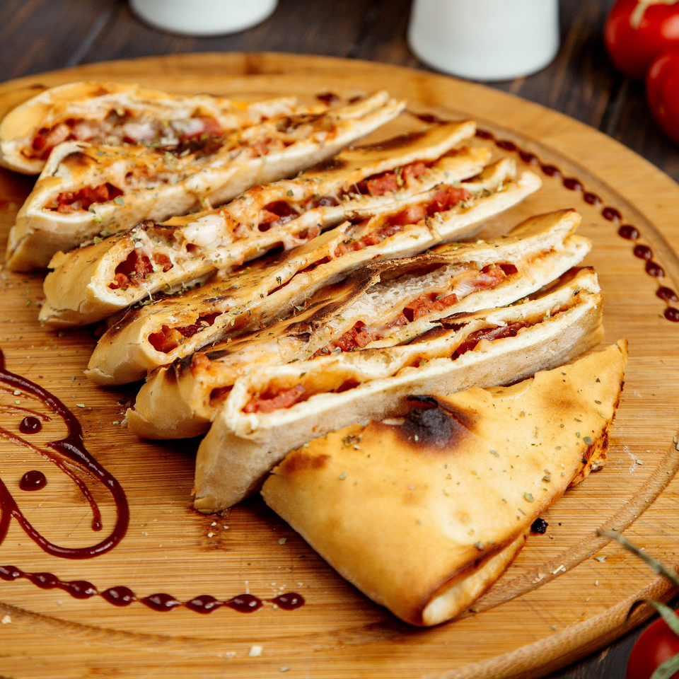 Sliced calzones filled with pepperoni and cheese, garnished with herbs on a wooden board.