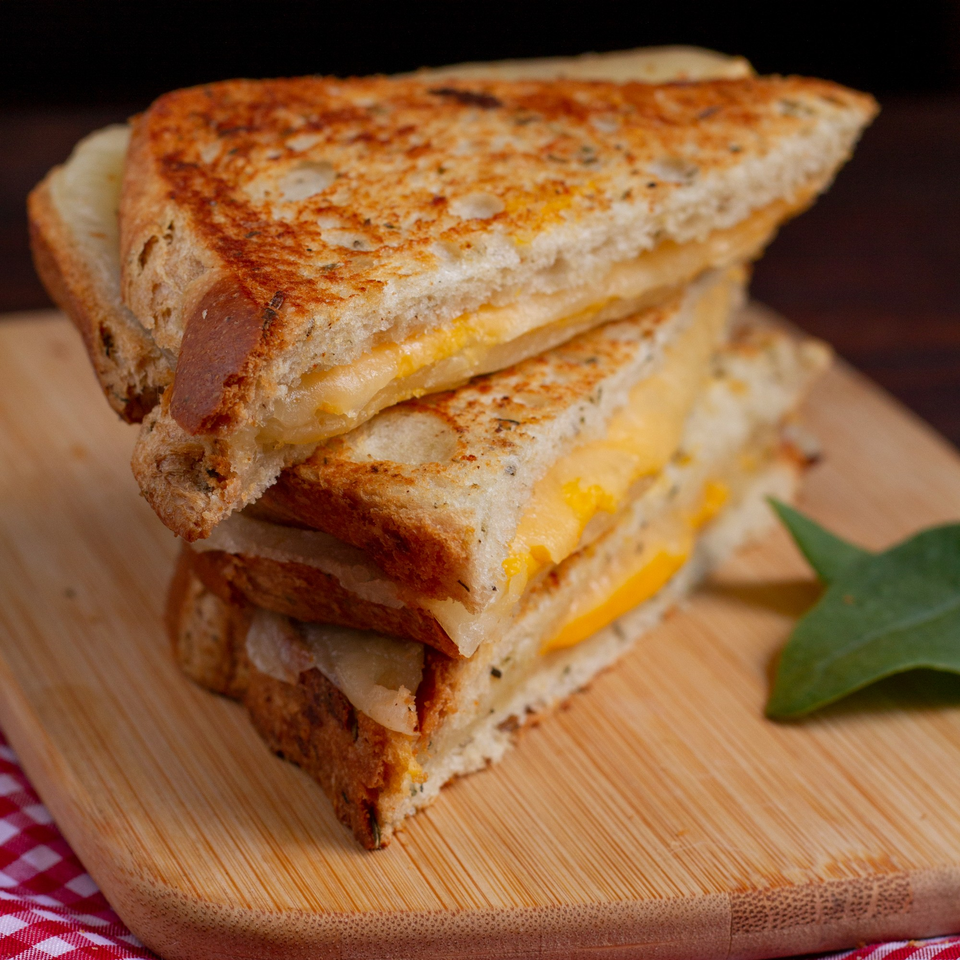 Stack of two grilled cheese sandwiches with melted cheddar on a wooden board.