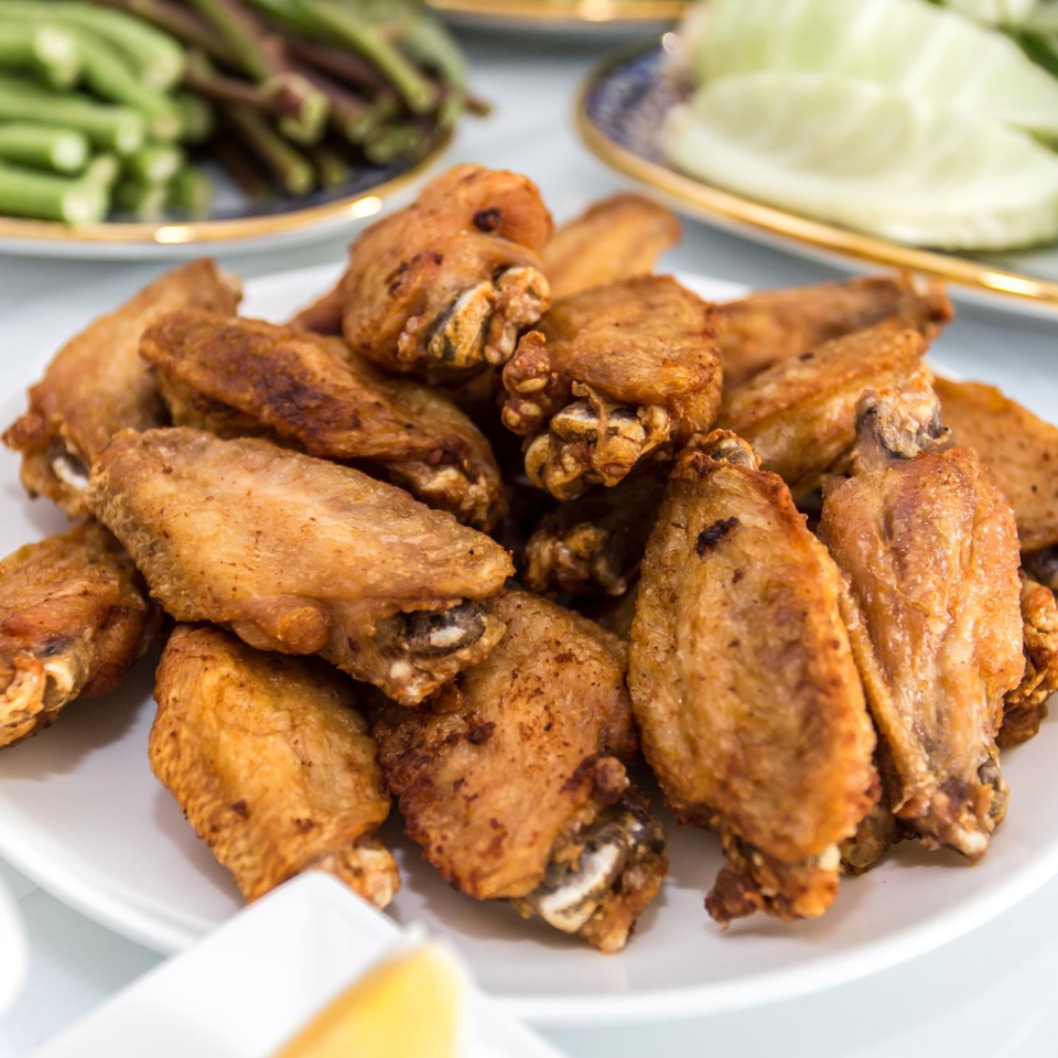 A white plate piled high with crispy, golden-brown fried chicken wings, with vegetables blurred in the background.